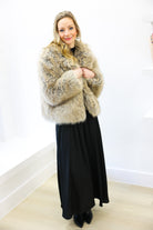 Woman wearing a fur coat and black dress against a white wall
