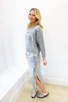 Woman wearing a gray sequin sweater and silver sequin skirt against a white background