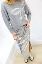 Person wearing a gray sequin sweater and silver sequin skirt with a white background