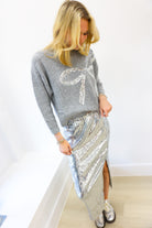 Woman wearing a gray sweater with a large white bow design and a silver sequin skirt.