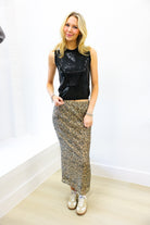 Woman wearing a black sleeveless top and patterned skirt against a white wall.