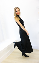 Woman wearing a black sleeveless dress standing against a white wall.
