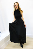 Woman wearing a black sleeveless dress standing indoors with a white background