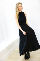 Woman wearing a black sleeveless dress against a white wall.