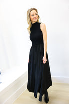 Woman wearing a black sleeveless dress against a white wall.