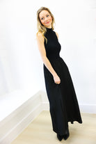 Woman wearing a black dress standing against a white wall.