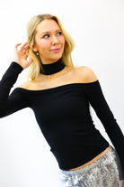 Woman wearing a black off-shoulder top and silver sequin skirt on a white background