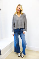 woman wearing grey sweater with sequin and collar detail paired with medium wash denim up against white wall