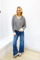 woman wearing grey sweater with sequins and white collar up against white wall