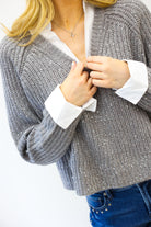 Person wearing a gray knitted cardigan over a white shirt with blue jeans on a white background