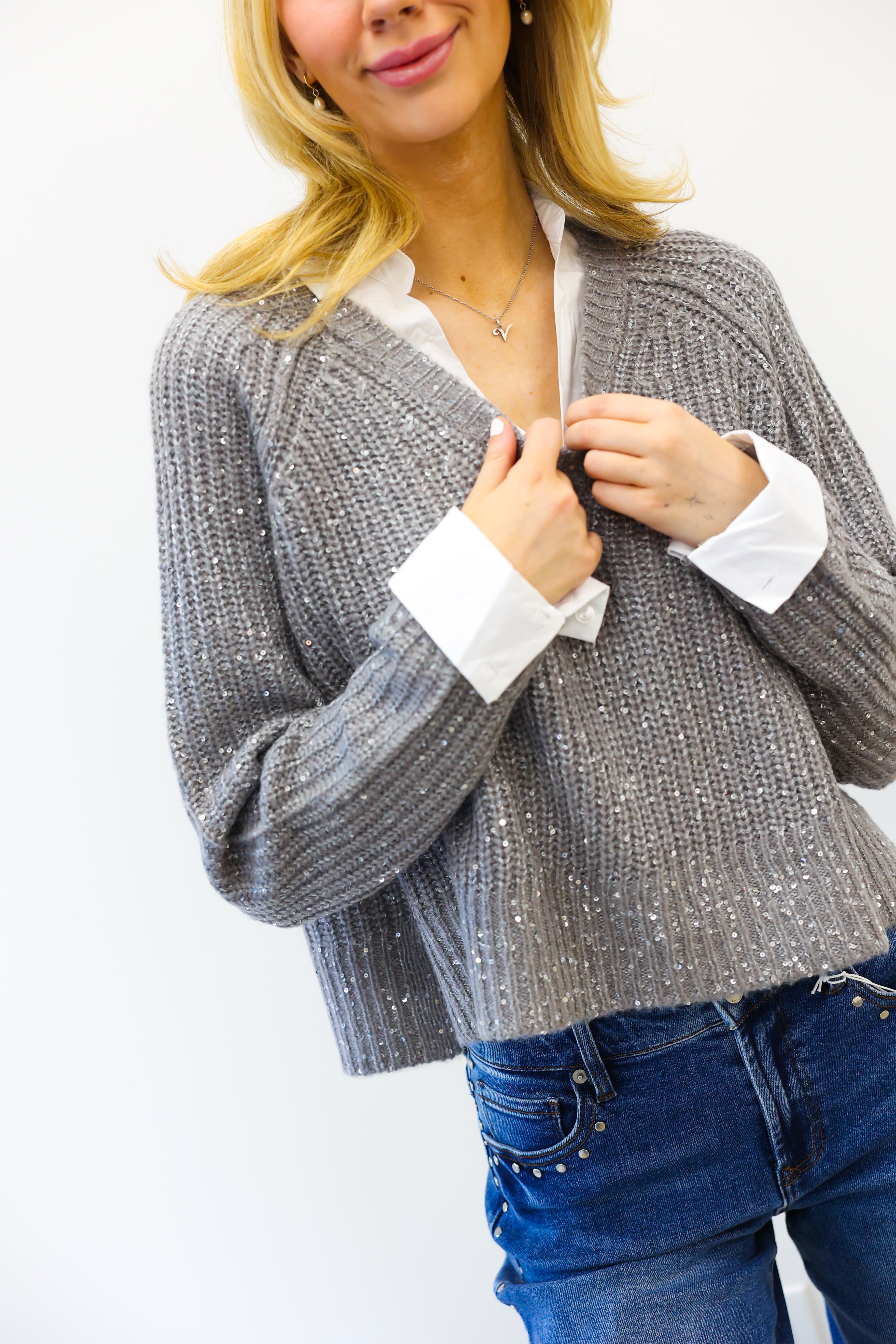 Woman wearing a gray knitted cardigan over a white shirt with blue jeans on a white background