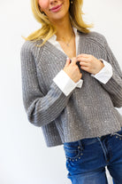 Woman wearing a gray knitted cardigan over a white shirt with blue jeans on a white background