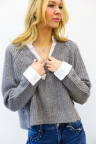 woman wearing grey sparkly sweater with white collar up against white wall
