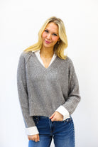 Woman wearing a gray sweater with a white shirt underneath on a white background