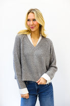 woman wearing grey sweater with sequins and white collar up against white wall