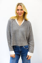 Woman wearing a sparkly gray sweater with a white collar and cuffs, standing against a white background.