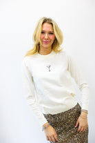 Woman wearing a white sweater with a small design on a plain background