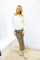 Woman wearing a white sweatshirt and patterned skirt standing against a white wall.