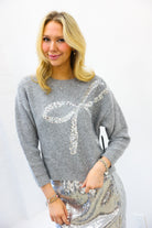 Woman wearing a gray sweater with a large sequin bow and a silver sequin skirt on a white background