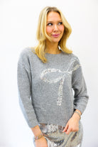 Woman wearing a gray sweater with a decorative silver design on a white background