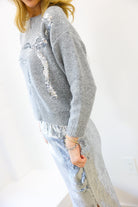 Person wearing a gray sequin sweater and pants on a white background