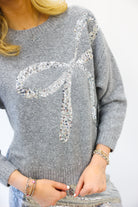 Gray sweater with a decorative bow design on a plain background