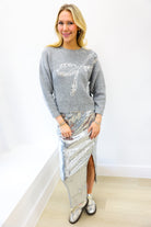 Woman wearing a gray sweater with sequin design and a silver sequin skirt on a white background