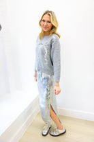 Woman wearing a gray sequin sweater and silver sequin skirt with white shoes on a plain background