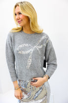 Woman wearing a gray sweater with sequin design on a white background
