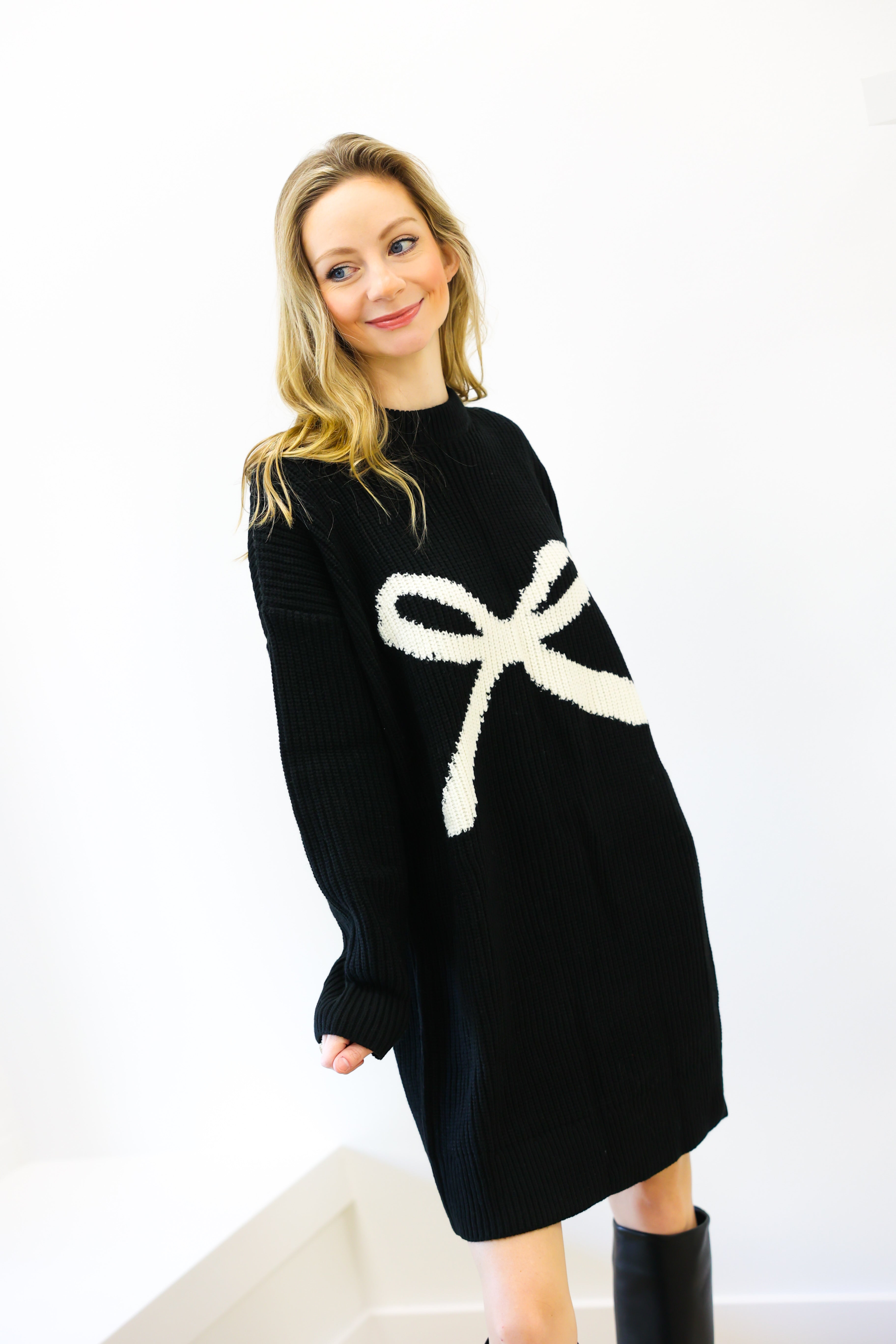Woman wearing a black sweater dress with a white bow design on a white background