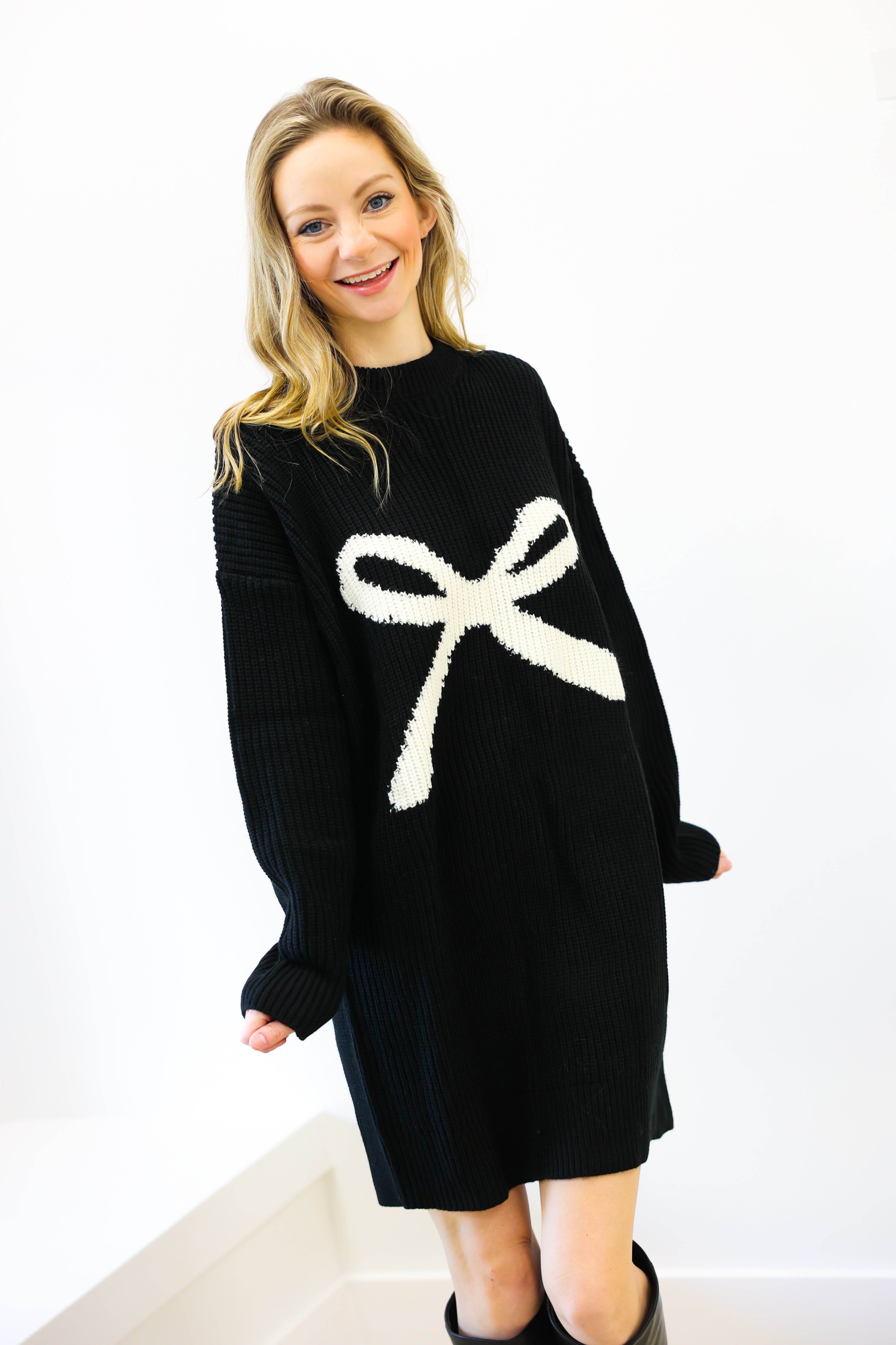 Woman wearing a black sweater dress with a white bow design on a white background