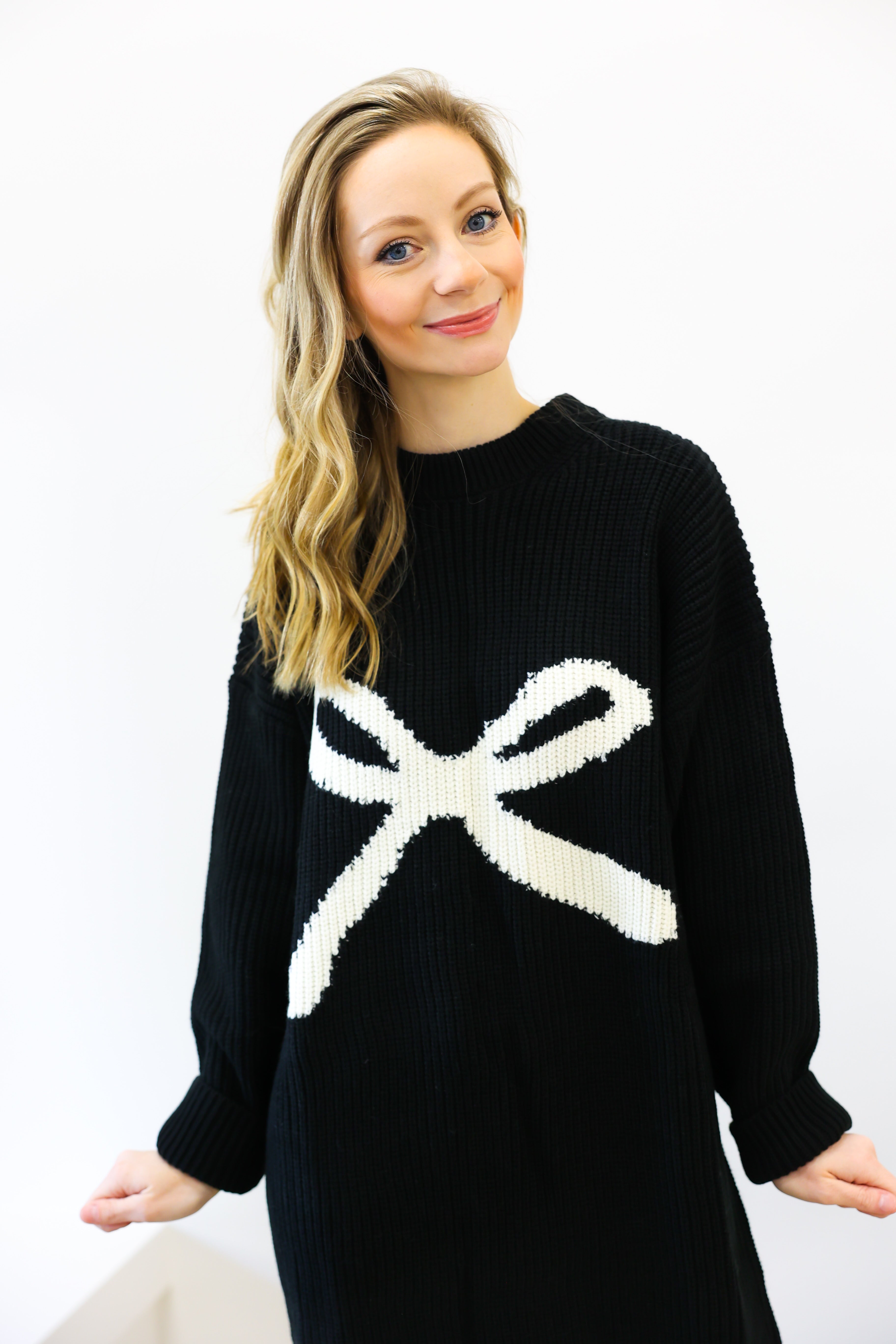 Woman wearing a black sweater with a white bow design on a white background