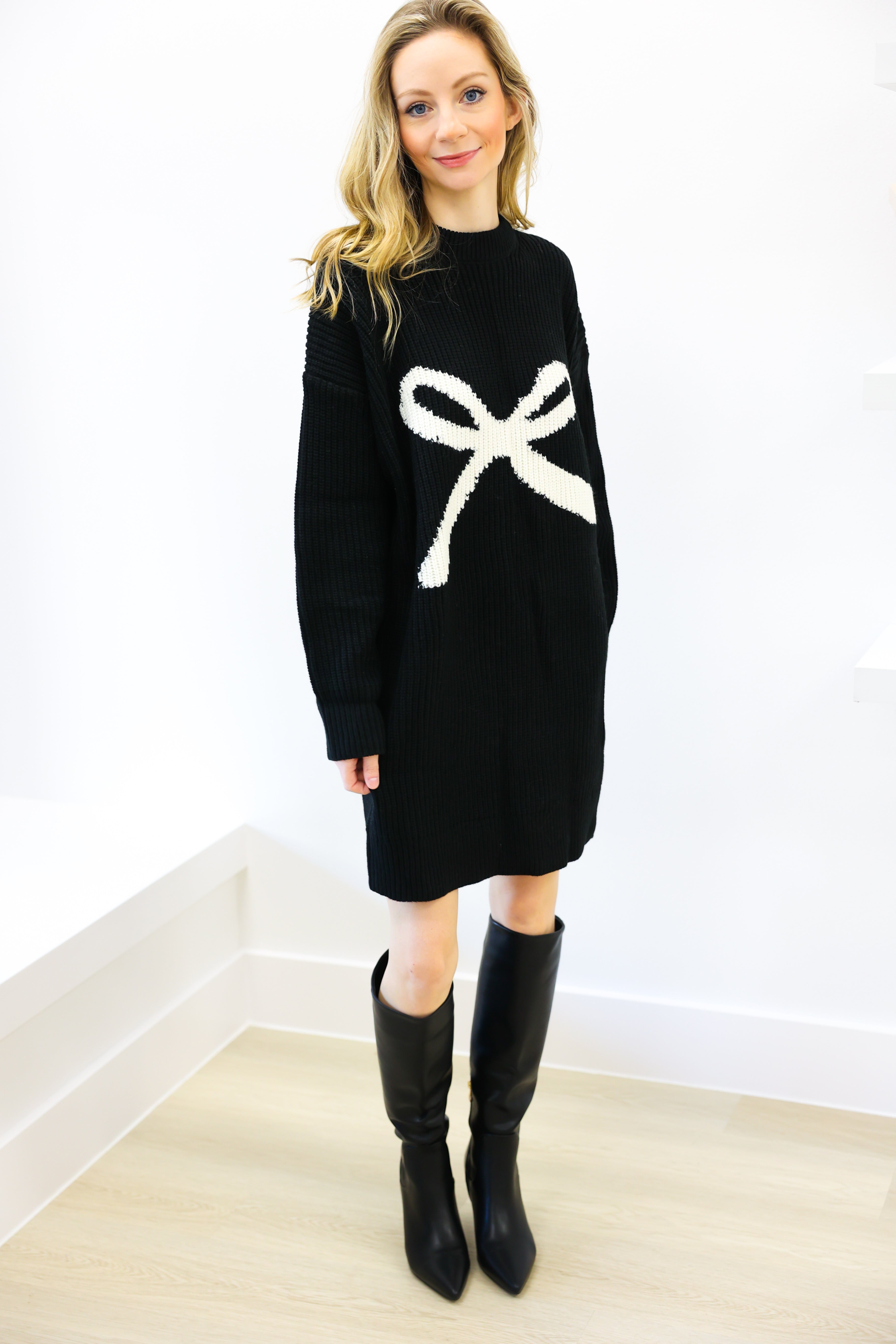 Woman wearing a black sweater dress with a white bow design against a white background