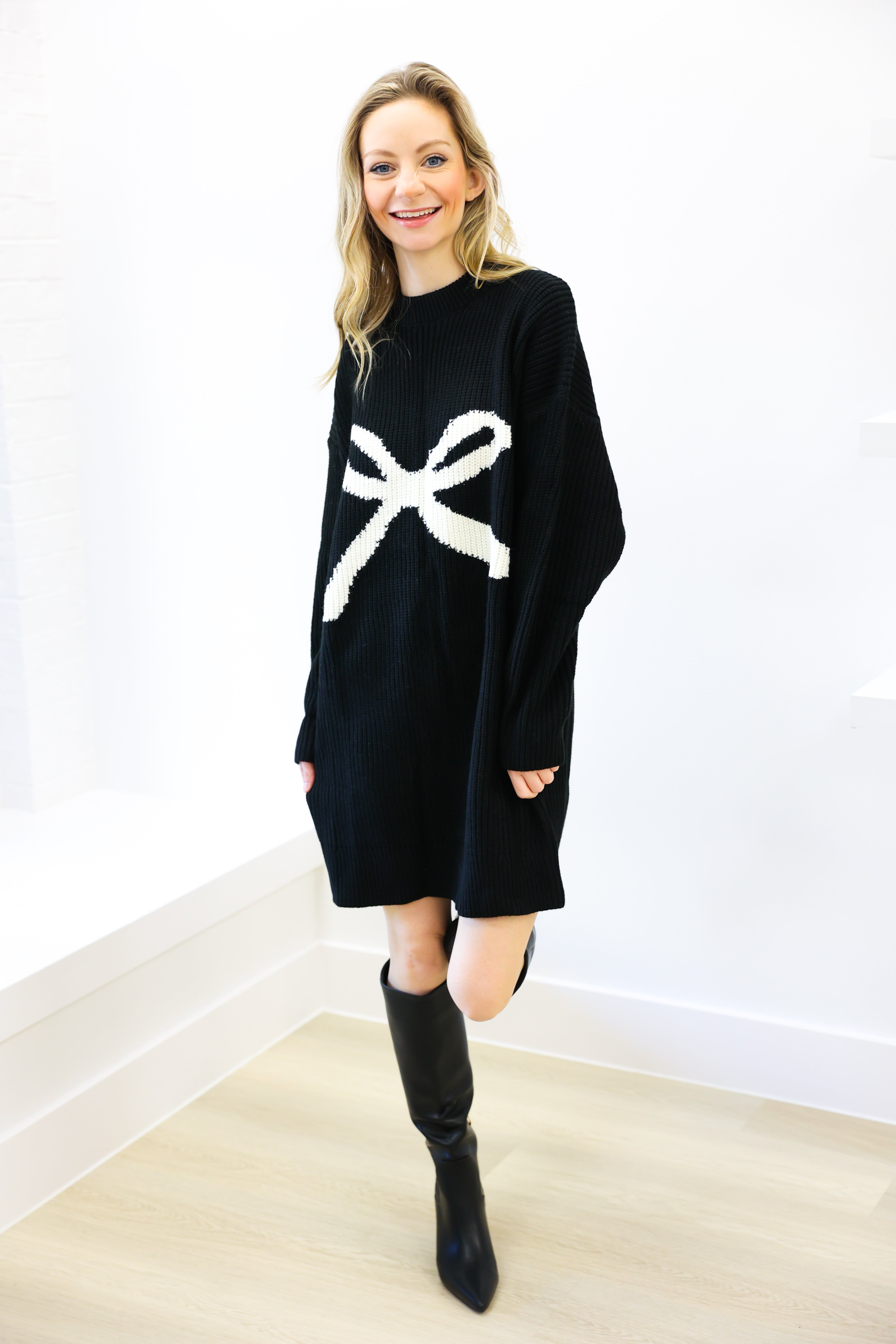 Woman wearing a black sweater dress with a white bow design on a white background