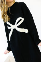 Black sweater with a white bow design worn by a person on a white background