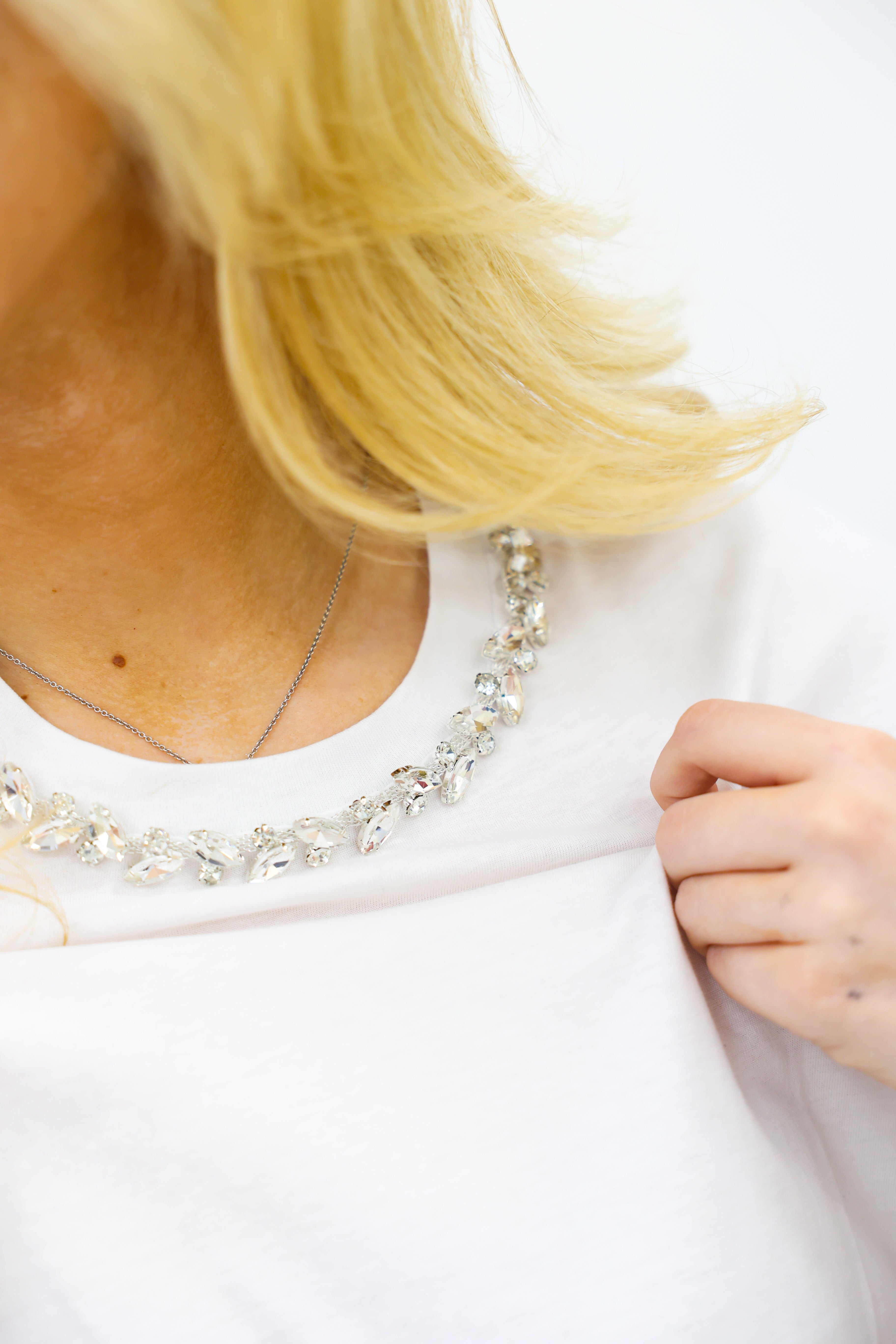 Close-up of a person wearing a white shirt with a necklace, focusing on the neckline.