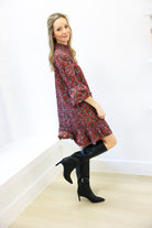 Woman wearing a floral dress and black boots against a white wall.
