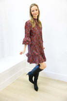 Woman wearing a floral dress and black boots standing against a white wall.