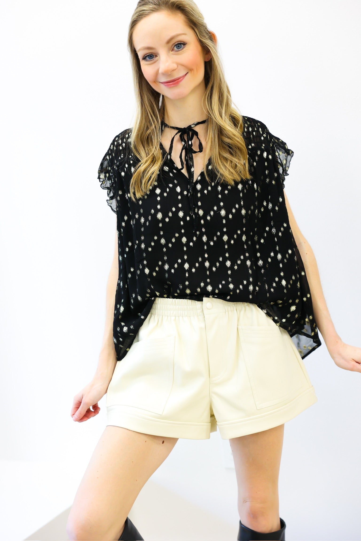 Woman wearing a black floral blouse and cream shorts on a white background