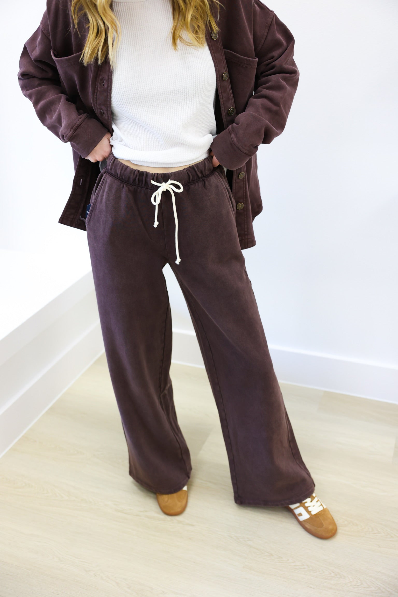 Person wearing a brown tracksuit with a white shirt underneath on a light wooden floor.