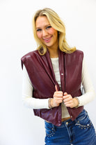 Woman wearing a maroon leather vest over a white long-sleeve shirt and blue jeans on a white background
