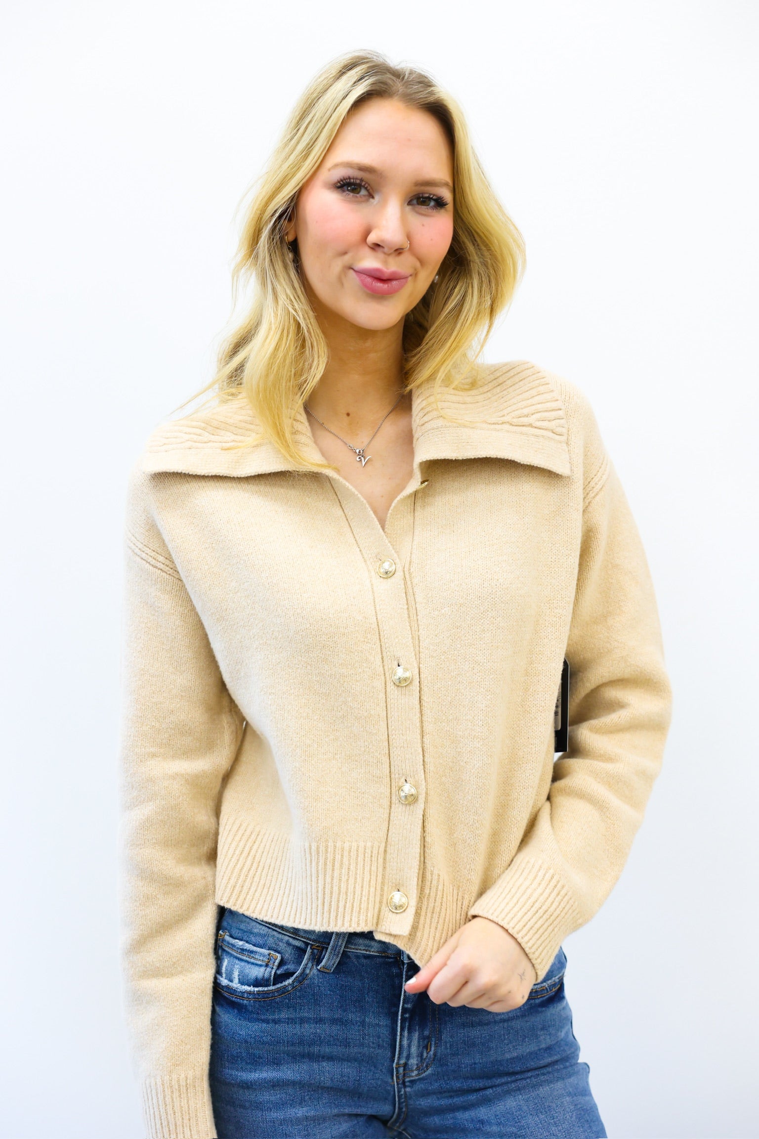 Woman wearing a beige cardigan and blue jeans on a white background