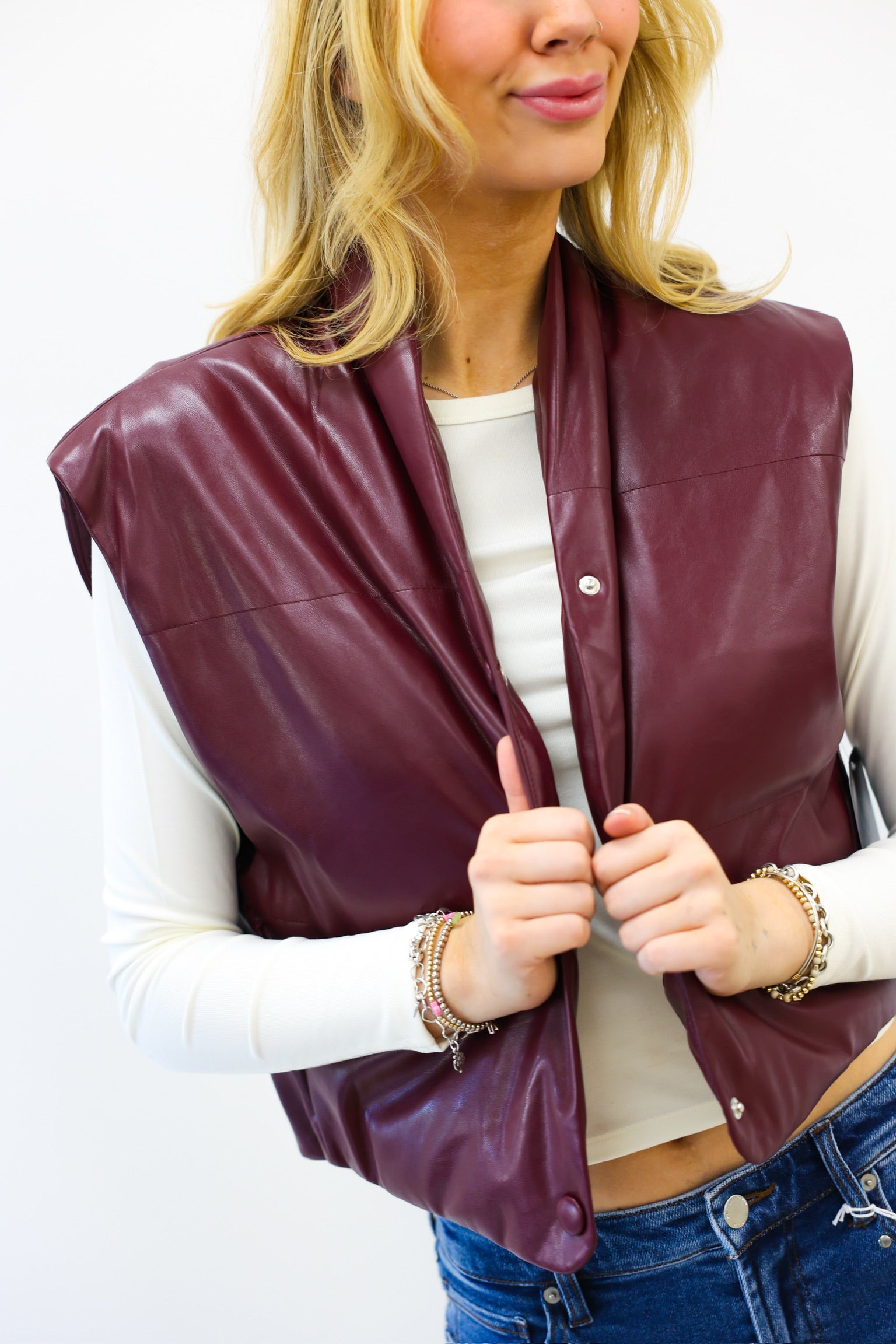 Woman wearing a burgundy leather vest over a white shirt with a plain background