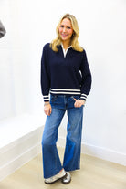 Woman wearing a navy sweater with white stripes and blue jeans against a white wall.