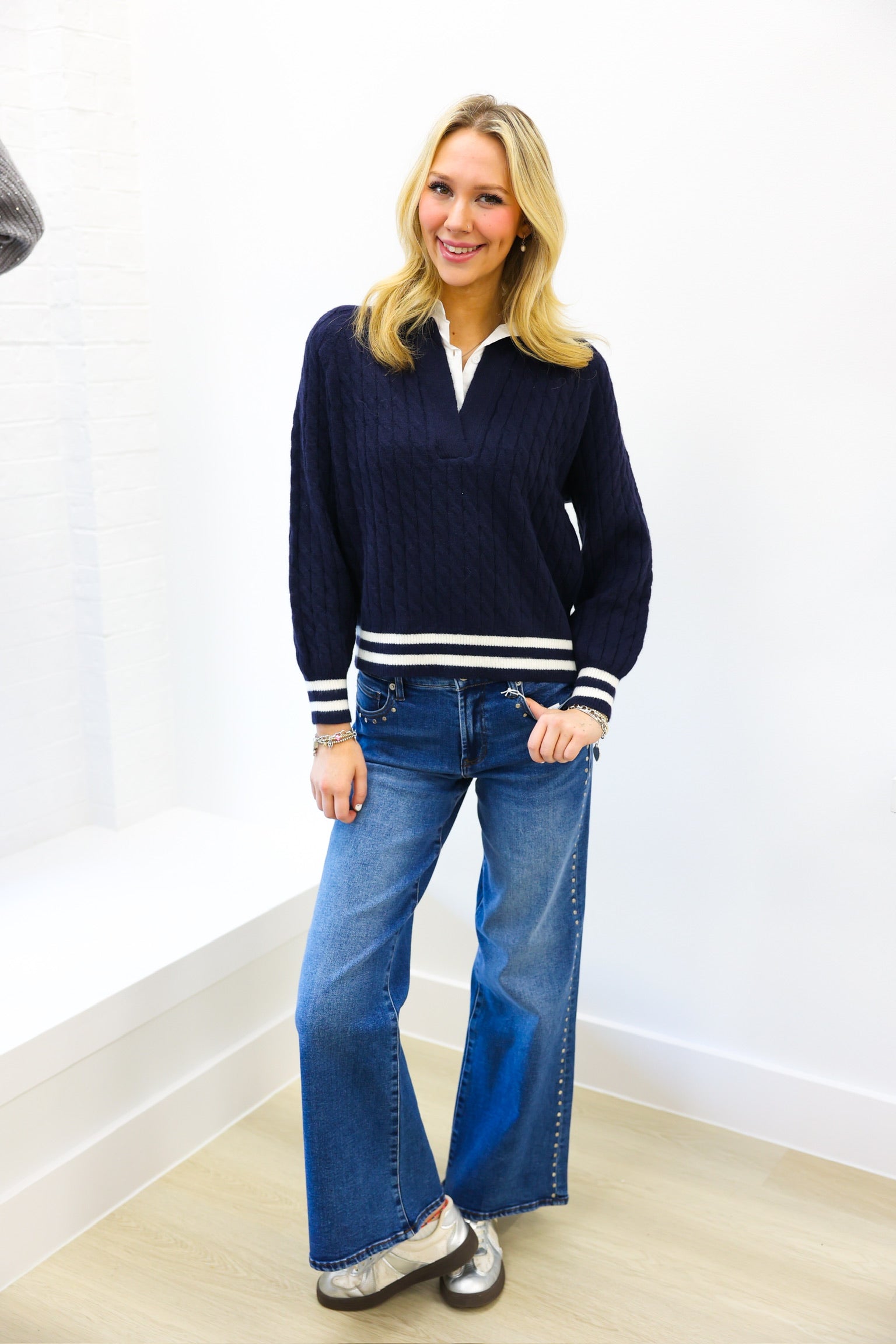 Woman wearing a navy sweater with white stripes and blue jeans against a white wall.