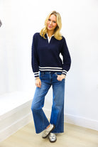 Woman wearing a navy sweater with white stripes and blue jeans against a white wall.