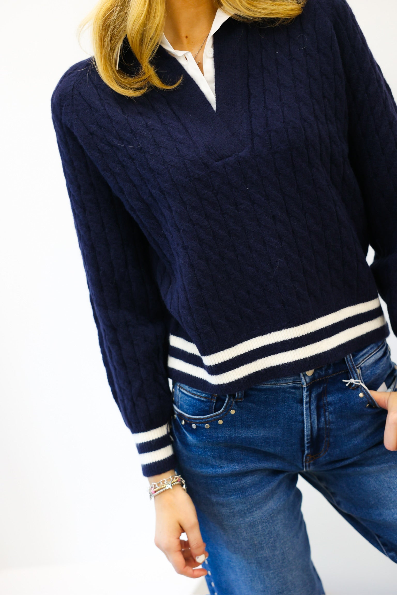 Person wearing a navy sweater with white trim and blue jeans on a white background
