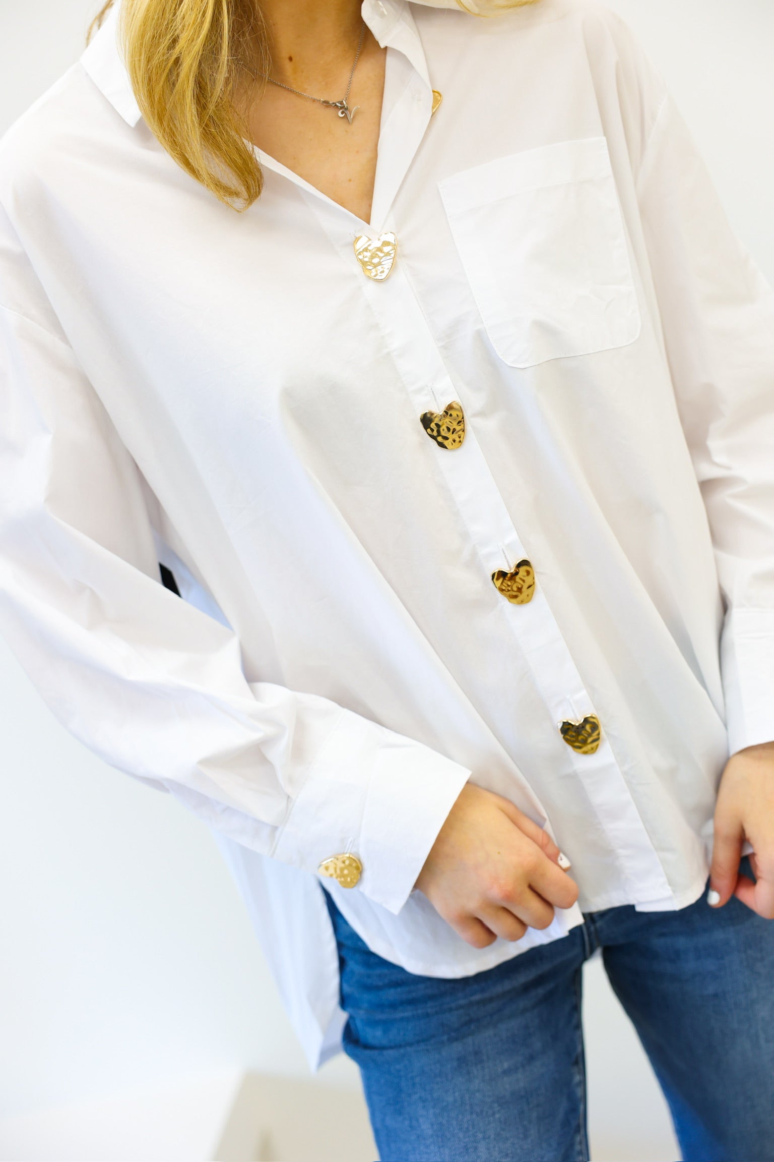 White blouse with gold buttons worn by a person, on a plain background