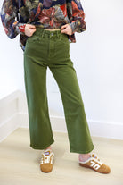 Person wearing green wide-leg jeans and a colorful patterned shirt on a white background