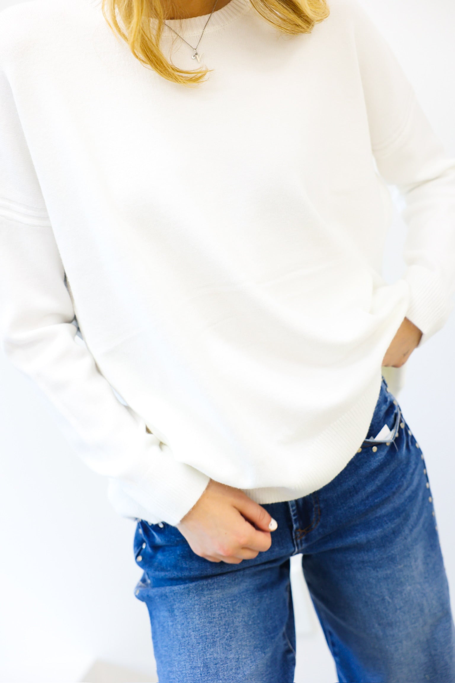 Person wearing a white sweater and blue jeans on a plain background